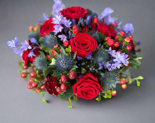 A dainty posy arrangement of red roses, blue thistle and Bluebells.