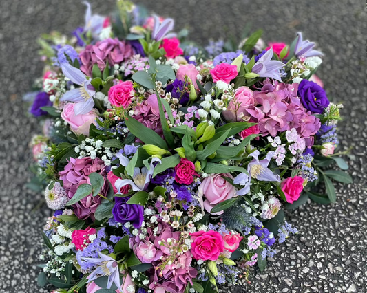 A beautiful heart shaped funeral arrangement. Creating using lots of fresh flowers in pink and purple colours.