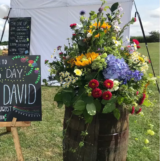 welcome board at a wedding complete with a beer barrel with colourful flowers on the top.