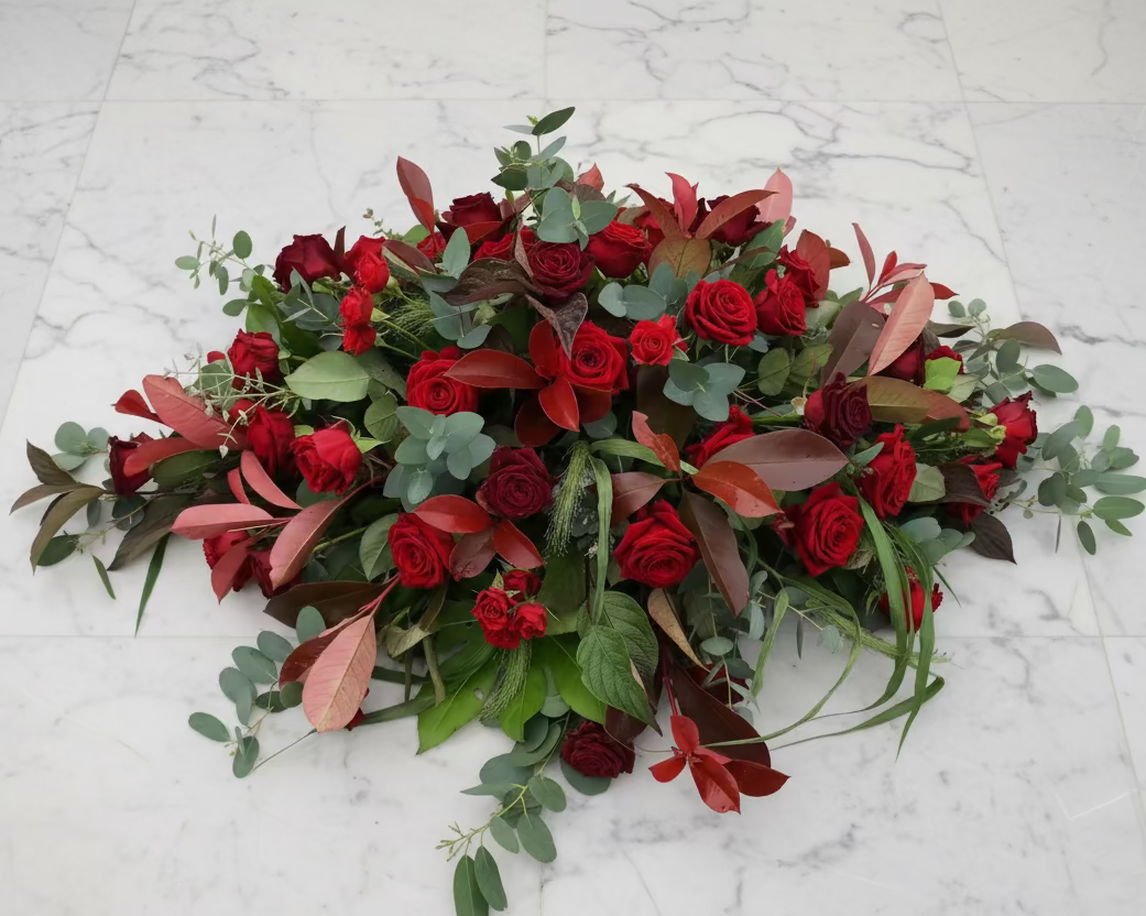 A funeral tribute of red roses with mixed foliage