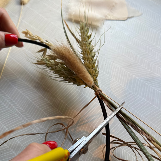 Person cutting dried grass with yellow-handled scissors.