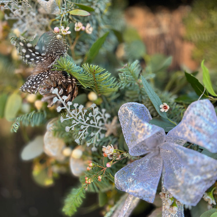 Decorative door wreath arrangement with greenery, ribbons, and feathers all in a silvery winter theme.