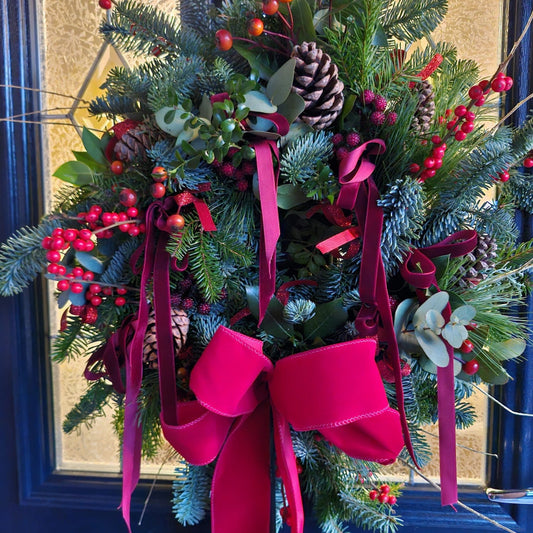 Christmas door wreath with greenery, berries, and pink ribbons on a door.