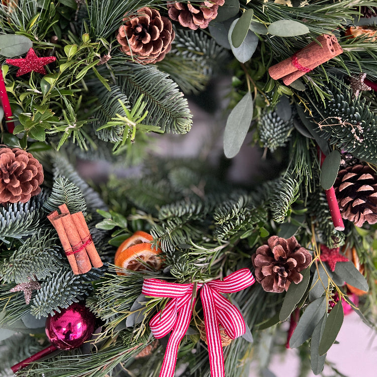 Christmas wreath with greenery, pinecones, cinnamon sticks, and a red ribbon.
