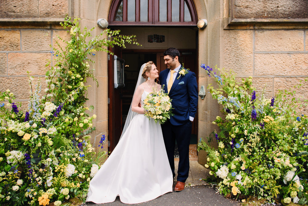 Wedding couple standing in front of a stone building with floral decorations.