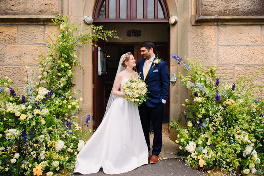Wedding couple standing in front of a stone building with floral decorations.