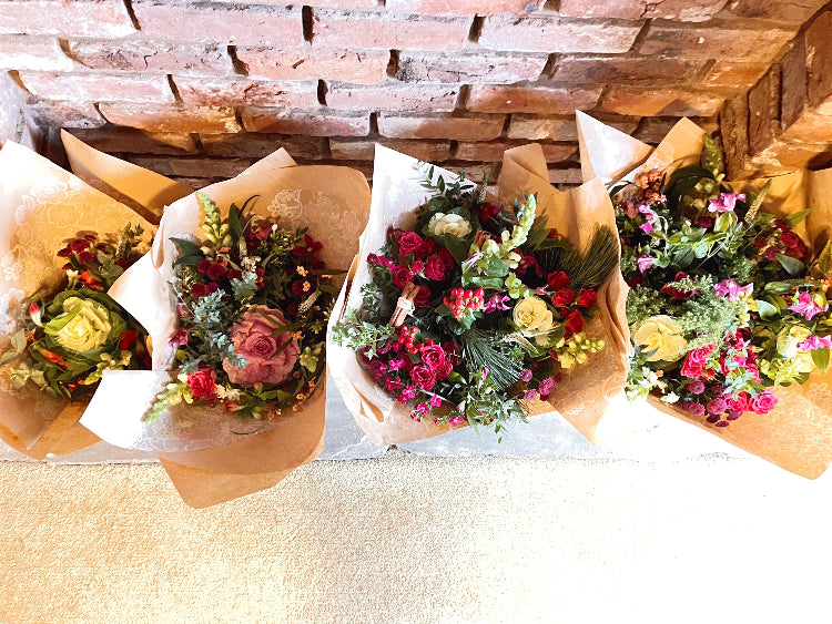 Four bouquets of flowers wrapped in brown paper against a brick wall.