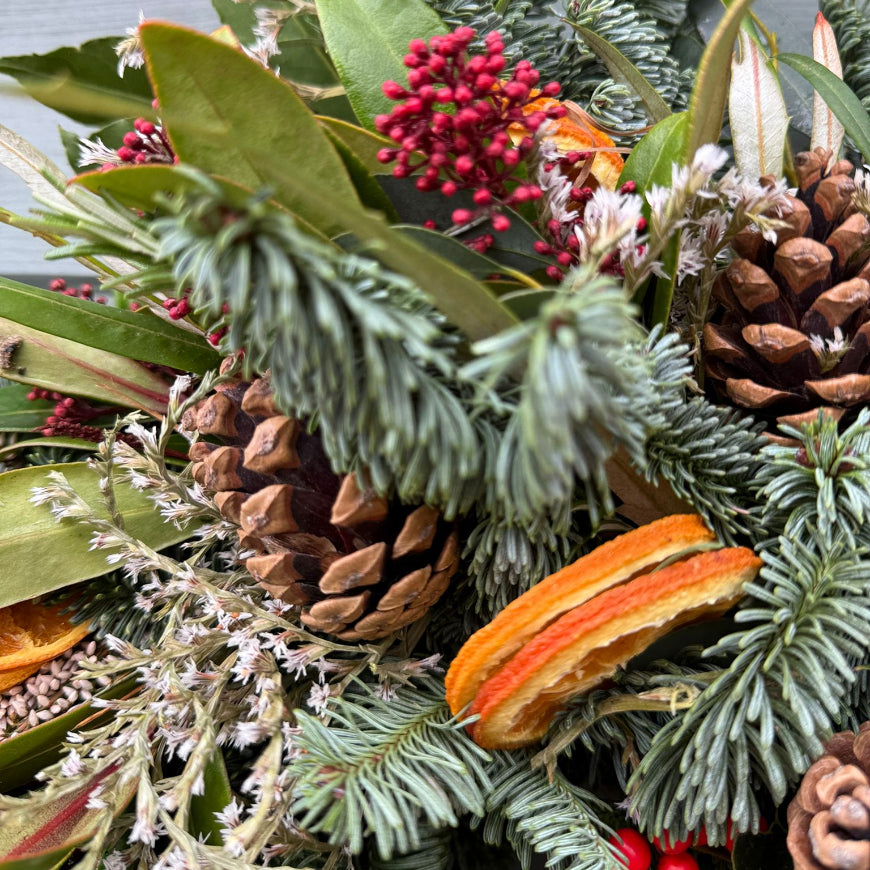 A close up picture of a natural style Christmas Wreath by Flower Farm Floristry. Picture includes Skimmia, Cones, Limonium, Nordman Fur, Ilex Berries, Limonium, Orange Slices and Bay