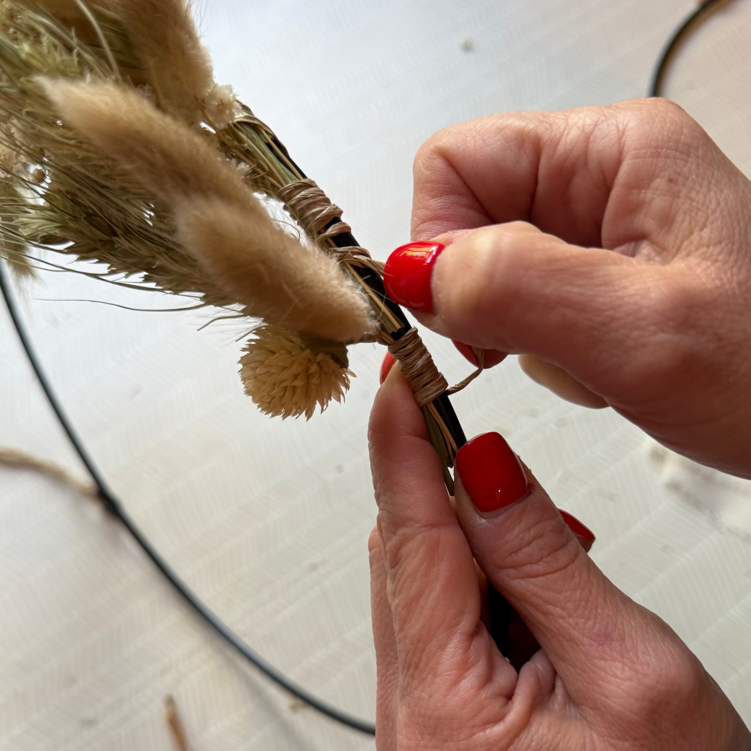 Person's hands attaching dried flowers and grasses to a wire frame