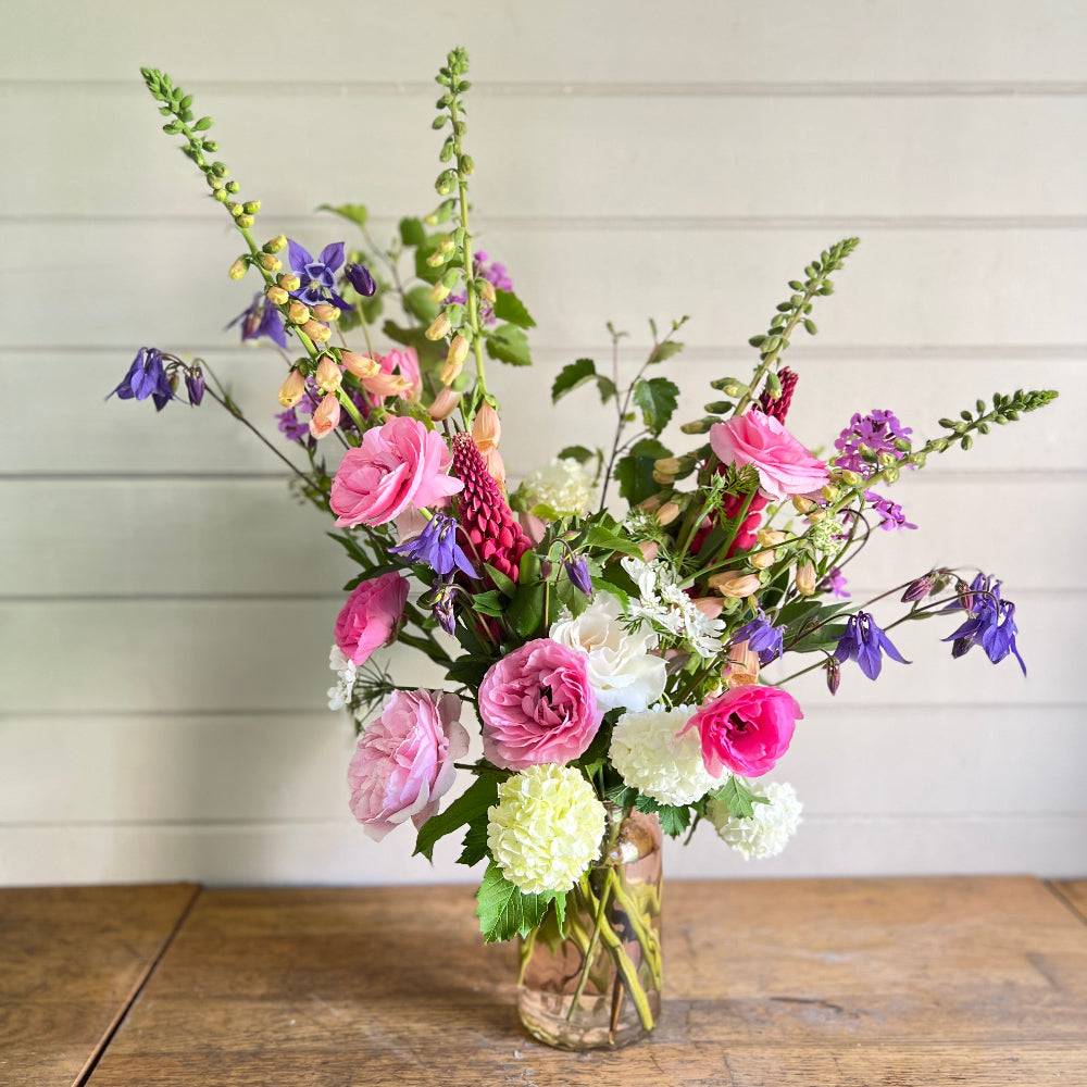 A beautiful vase filled with fresh, country style flowers in pinks and purples.