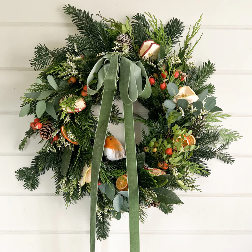 Decorative wreath from flower farm floristry with greenery, fruits, and ribbon. Green velvet ribbon, Robin, Limonium