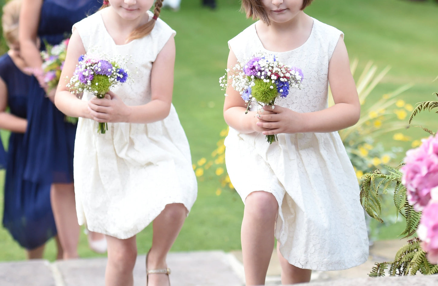 two flower girls in white dresses carrying posies of flowers.