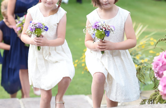 two flower girls in white dresses carrying posies of flowers.