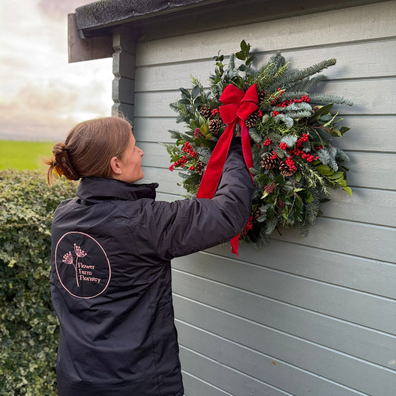 Alison Matthews hanging our gorgeous new fresh Christmas Door wreath with a large red bow, including bay, nordnamn fur, Rosemary, Skimmia, Ilex Berries and fir cones