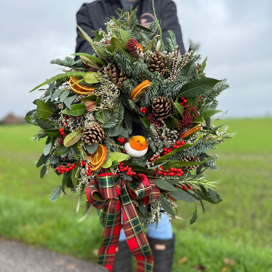 A natural style Christmas wreath with a robin and a tartan ribbonfrom Flower Farm Floristry, held by Alison Matthews in front of our beautiful view from the farm. 