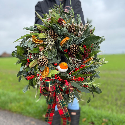 A natural style Christmas wreath with a robin and a tartan ribbonfrom Flower Farm Floristry, held by Alison Matthews in front of our beautiful view from the farm. 