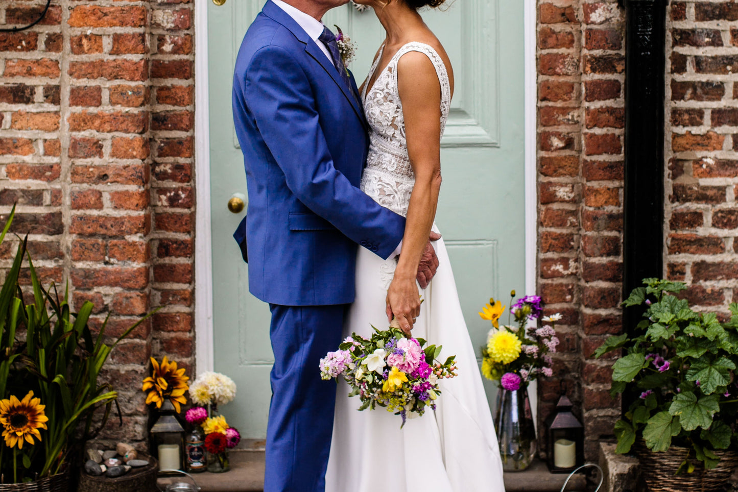 A bride and groom embracing each other with a kiss with colourful flowers around them.