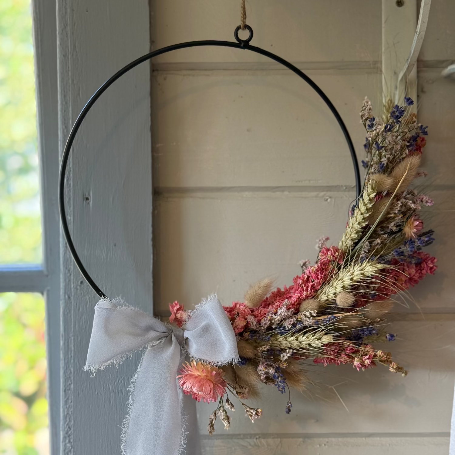 Decorative wreath with dried flowers and a white bow hanging on a door.