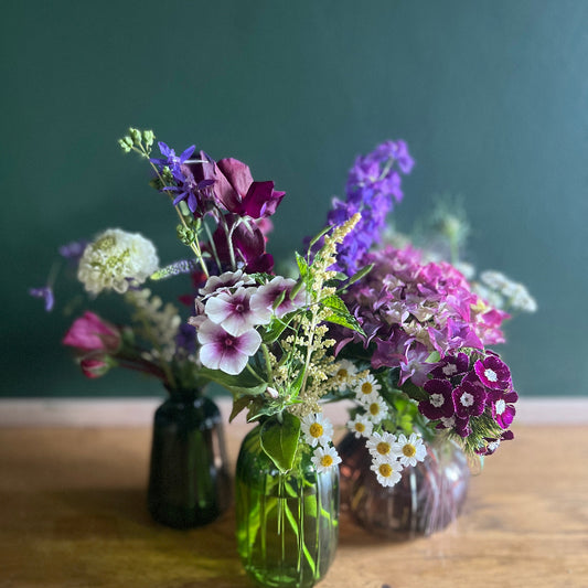 Three small vases with colorful flowers on a wooden surface against a dark green background