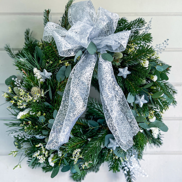 Christmas wreath with greenery, white flowers, and a silver bow.