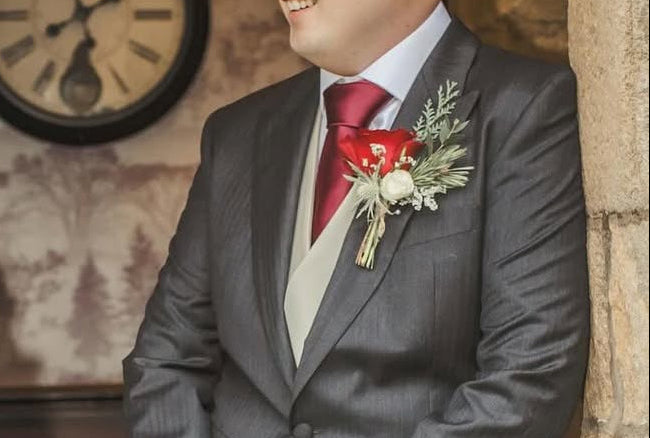A groom wearing a grey suit wearing a red rose buttonhole
