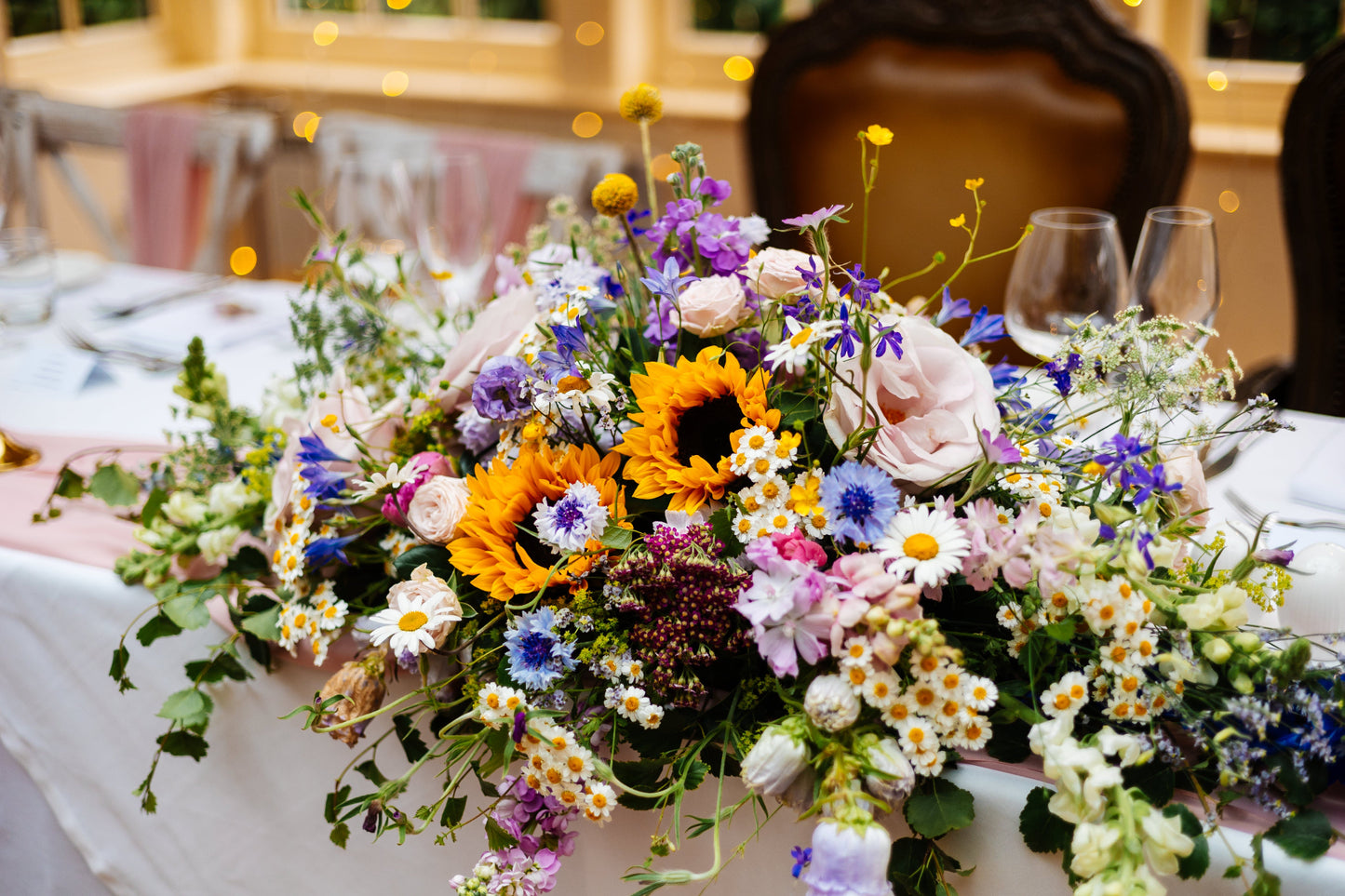 traditional long and low arrangement for a ceremony or top table in bright flowers for a June wedding at Mitton Hall in Lancashire. 

Including Sunflower, Achilea, Cirnflowers, Daisies, Snapdragon, Rses, Buttercups, Ammi, Craspedia, Stocks, Limonium. 
Wildflower style arrangement. 

Photography by Fairclough Studios