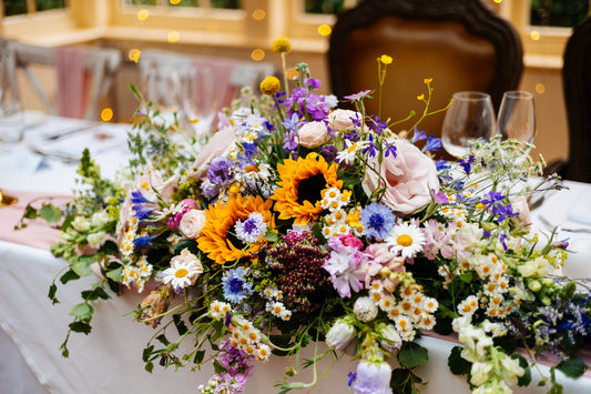traditional long and low arrangement for a ceremony or top table in bright flowers for a June wedding at Mitton Hall in Lancashire. 

Including Sunflower, Achilea, Cirnflowers, Daisies, Snapdragon, Rses, Buttercups, Ammi, Craspedia, Stocks, Limonium. 
Wildflower style arrangement. 

Photography by Fairclough Studios